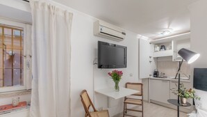 A compact room with a kitchenette, a dining area with a table and chairs, a mounted TV, and a window with a curtain. - GuestHost - Basic Studio - 350 m far from Fontana di Trevi (Roma)