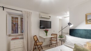 A bedroom with a bed, a desk with a chair, a TV, an air conditioner, and a window with curtains. - GuestHost - Basic Studio - 350 m far from Fontana di Trevi (Roma)