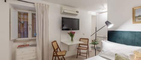 A bedroom with a bed, a desk with a chair, a TV, an air conditioner, and a window with curtains.