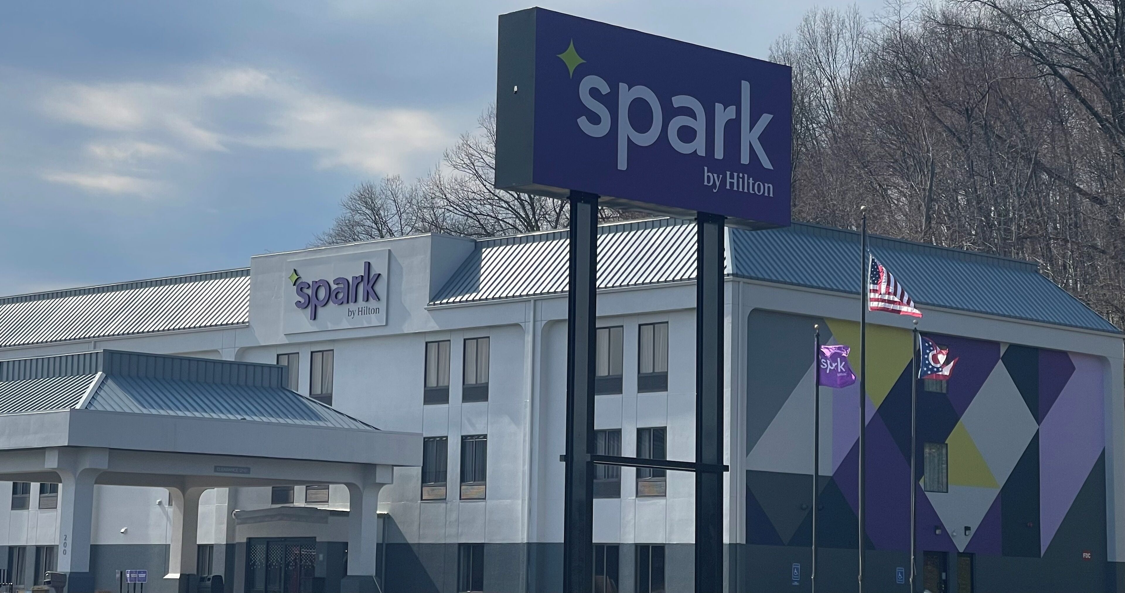 A hotel named 'Spark by Hilton' with a modern design, featuring a prominent sign and a distinctive geometric facade.
