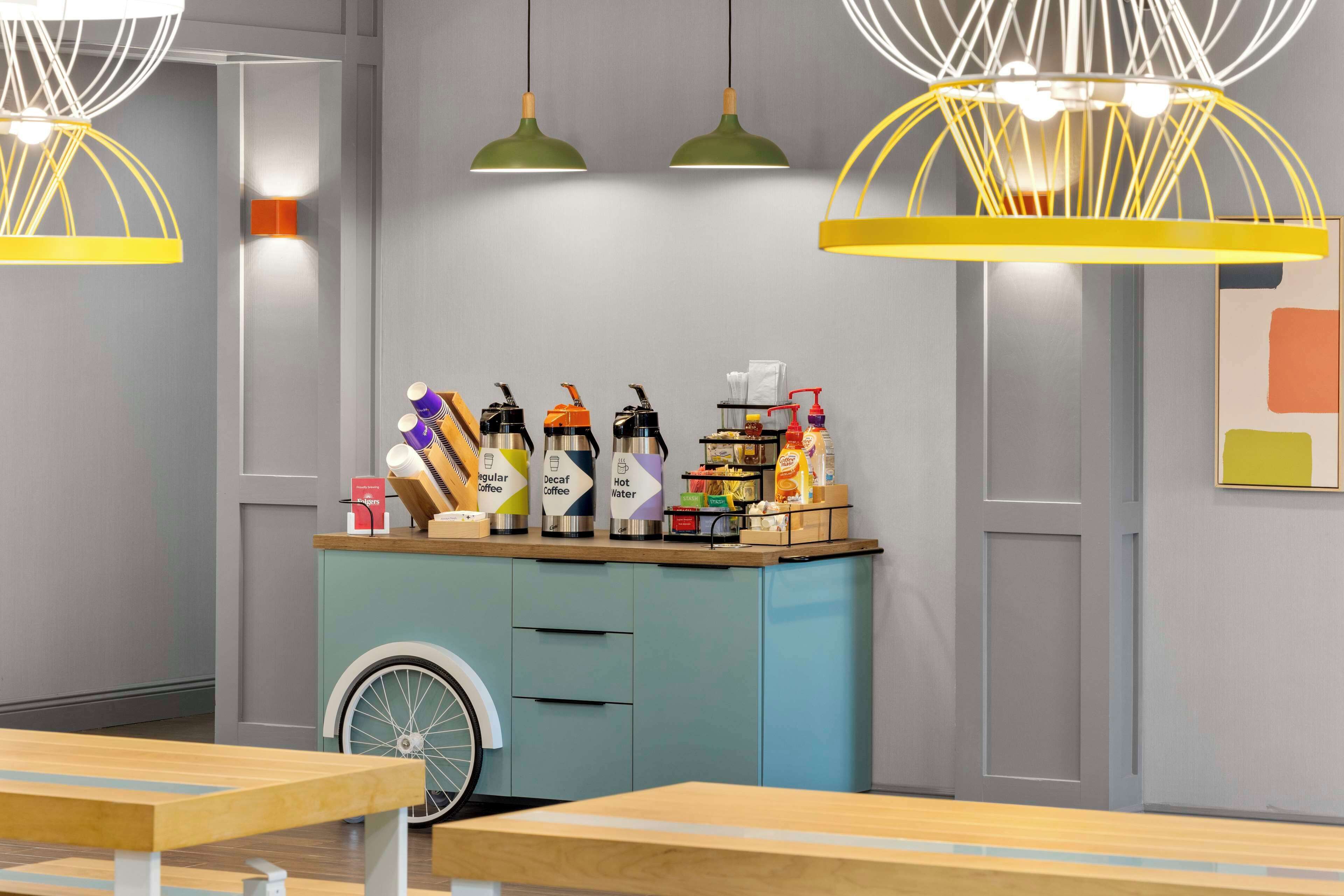 L'intérieur d'un café moderne, avec un comptoir de couleur turquoise, divers distributeurs de café et de thé, et des lampes suspendues.