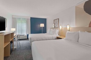 A hotel room with two beds, a desk with a TV, a chair, and a window with curtains.