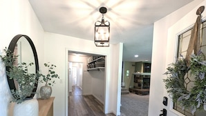 A hallway with a wooden floor, a large mirror, a potted plant, and a door with a decorative wreath. - Peaceful Gathering Place with 12 bedrooms and 7 bathrooms. Game Tables and Pool! (South Bend)