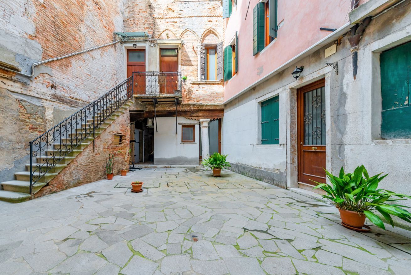 A courtyard with a stone floor, a staircase, and potted plants.