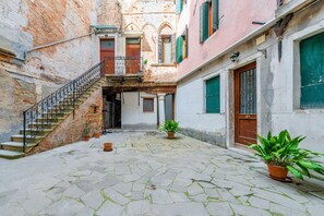 A courtyard with a stone floor, a staircase, and potted plants.