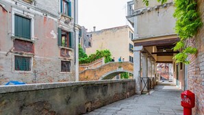 A narrow street with a bridge, buildings with balconies, and a pigeon on the ground. - GuestHost - Apartment located on the first floor of an ancient building without a lift.Splendid view of the canal from where the typical Venetian gondolas pass.It accommodates 4 people in 85 square meters of space with two double bedrooms.We are located  (Venezia)