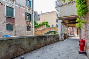 A narrow street with a bridge, buildings with balconies, and a pigeon on the ground.