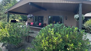A covered patio area with outdoor seating, a grill, and hanging flower baskets. - Seneca Lake View Retreat sits secluded on a 2 acre lot. (Himrod)