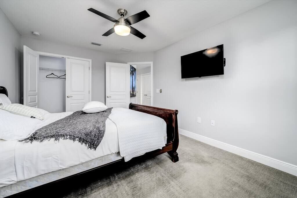 Une chambre à coucher avec un lit, un ventilateur de plafond, un téléviseur fixé au mur et une armoire contenant des vêtements suspendus.