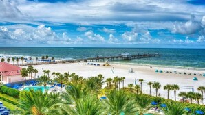 Ein Strandresort mit Pool, Palmen und einem Steg, der ins Meer führt.