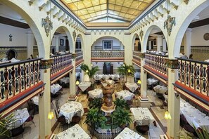 A spacious, well-lit atrium with multiple dining tables arranged around a central fountain, surrounded by arches and decorative railings. - South Tampa's Bougie Vacation Rental 4/3 (Tampa)