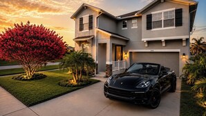 Ein zweistöckiges Haus mit Garage, Auffahrt und einem schwarzen Cabrio vor der Tür.