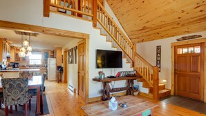 A spacious living area with a wooden staircase, a dining table with chairs, a television, and a kitchen in the background. - Rustic Pagosa Springs Cabin w/ Hot Tub + Game Room (Pagosa Springs)