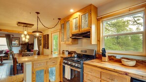A kitchen with wooden cabinets, a stove, and a large window. - Rustic Pagosa Springs Cabin w/ Hot Tub + Game Room (Pagosa Springs)