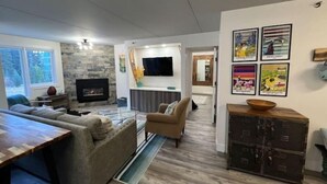 Een moderne woonkamer met een stenen openhaard, een flatscreen televisie en een eethoek met een houten tafel en stoelen.