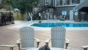 Een zwembadgedeelte met een vuurkuil, Adirondack-stoelen en een houten terras.
