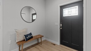 A hallway with a black door, a round mirror, a bench with a welcome pillow, and a light switch on the wall. - The Dells Domain (Wisconsin Dells)
