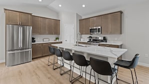 A modern kitchen with stainless steel appliances, wooden cabinets, and a marble island with bar stools. - The Dells Domain (Wisconsin Dells)