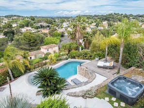 A swimming pool with a hot tub, surrounded by lush greenery and a view of a residential area.