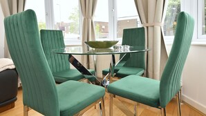 Een eethoek met een glazen tafel, omringd door vier groene bekleden stoelen.