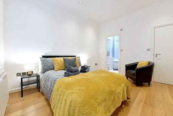 A bedroom with a bed, bedside table, lamp, chair, and a door leading to a bathroom.