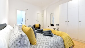 Een moderne slaapkamer met een groot bed, een stoel, een kledingkast en een spiegel.
