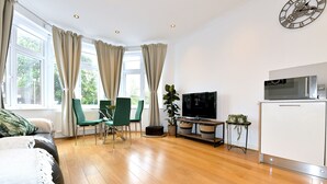 Een moderne woonkamer met een bank, groene stoelen, een televisie en een kast.
