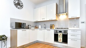 Een moderne keuken met witte kasten, een roestvrijstalen oven, een magnetron en een klok aan de muur.
