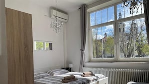 Et soveværelse med et stort vindue, en radiator, en lysekrone og en seng med håndklæder.