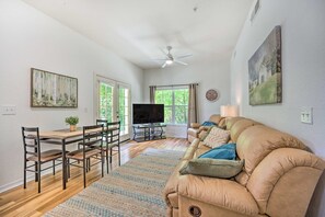 A spacious living room with a large beige sofa, a dining table with chairs, a TV, and artwork on the walls.