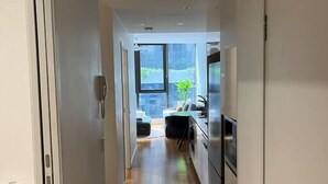 A narrow hallway with a wooden floor leading to a kitchen area with stainless steel appliances.