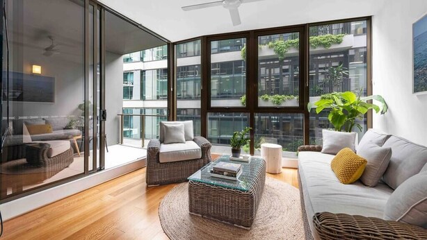 A modern living room with a large glass door, a ceiling fan, a sofa, a coffee table, and a view of a building with balconies.