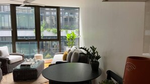 A modern living room with a round table, comfortable seating, and large windows offering a view of the city.
