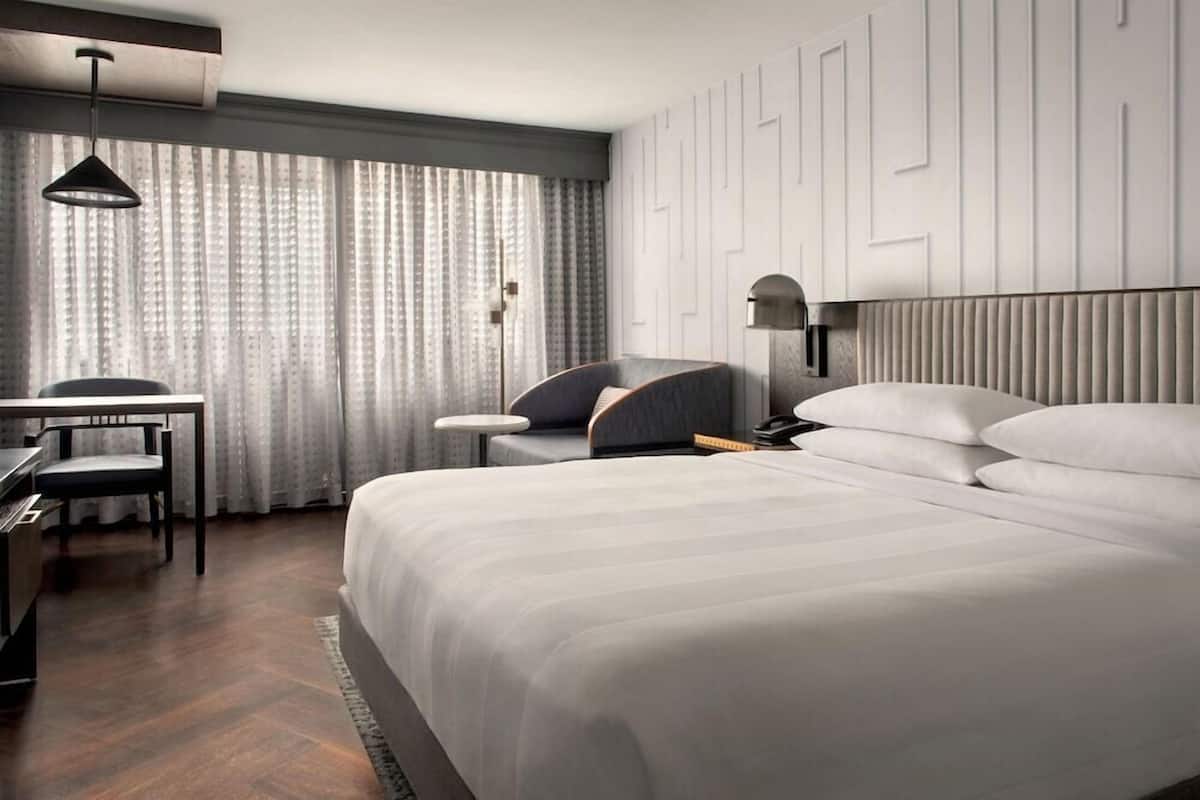 Una habitación de hotel moderna con una cama grande, un escritorio, una silla y una lámpara.