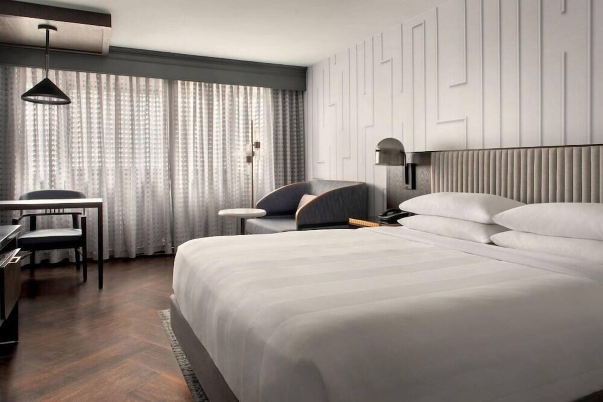 Moderni hotellihuone, jossa on suuri sänky, työpöytä, tuoli ja lamppu.