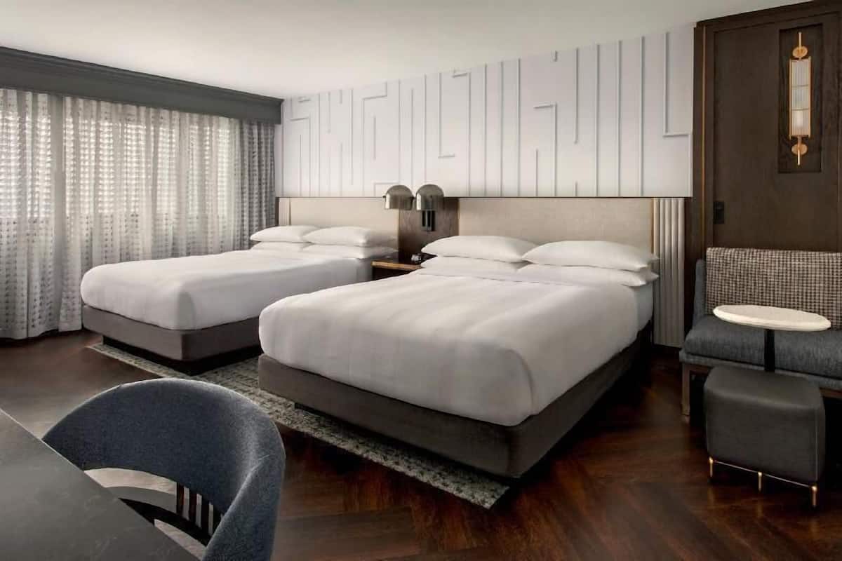 Habitación de hotel con dos camas, un escritorio, una silla, una mesita y una lámpara de pared.
