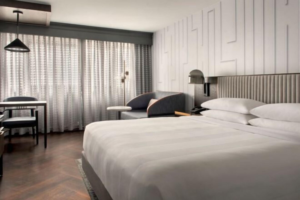 A hotel room with a large bed, a desk, a chair, and a window with curtains.