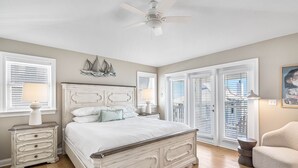 A bedroom with a white bed, wooden floor, and a ceiling fan.
