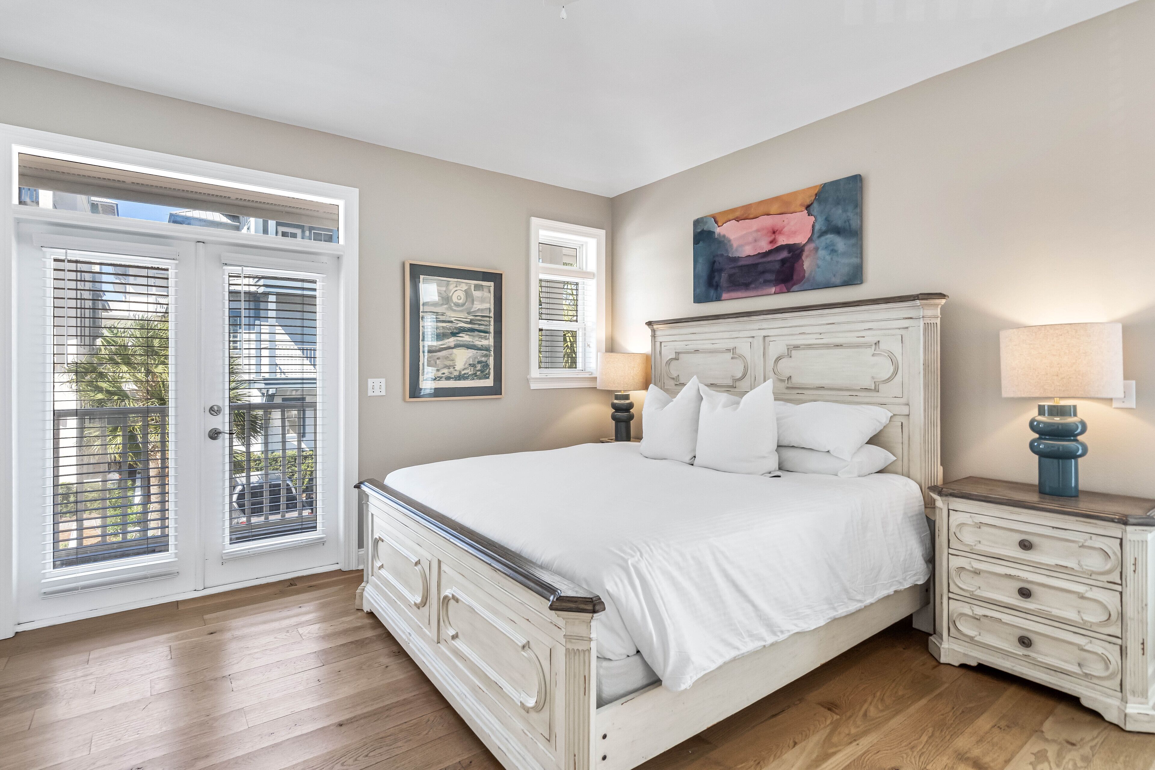 A bedroom with a large bed, a nightstand, a lamp, and a window with blinds.