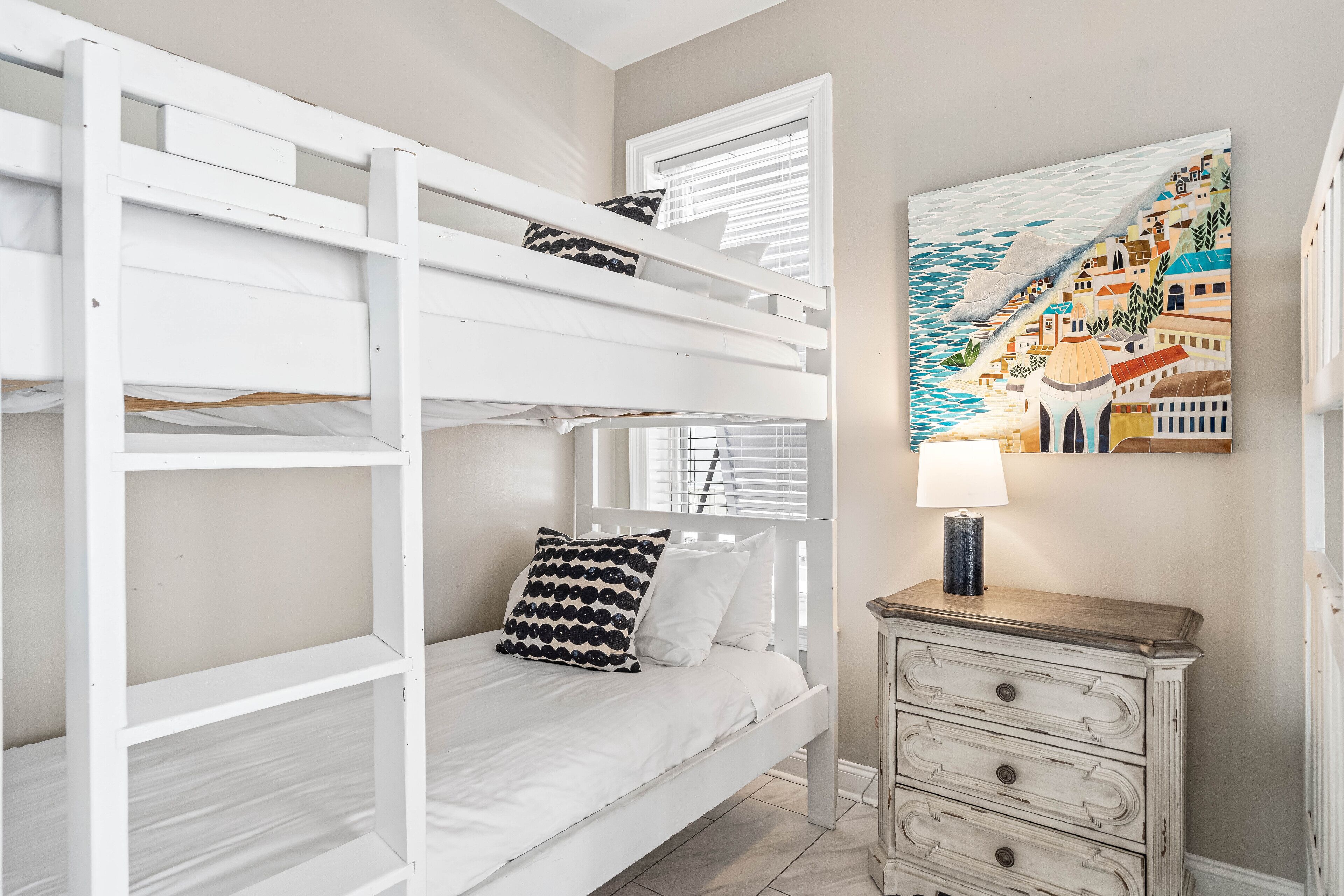 A bunk bed with two pillows, a small wooden nightstand with drawers, and a wall-mounted lamp.