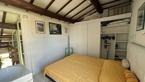 Een slaapkamer met een bed, een klein krukje, een douchegedeelte en een witte inloopkast.