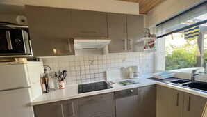 Een moderne keuken met grijze kastjes, een wit aanrecht, een ingebouwde magnetron en een raam met uitzicht op groen.
