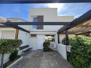 A covered patio area with a bench, a small door, and an air conditioning unit. - Villa avec deux chambres face à la plage de la Roquille (LE CAP D AGDE)