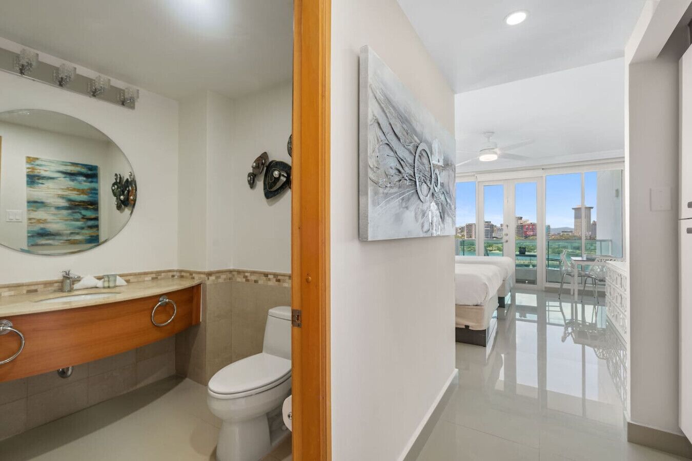 A modern bathroom with a large mirror, a toilet, and a sink. There is a balcony with a view of the city.