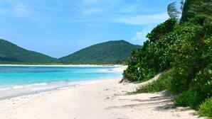 A beach with clear turquoise waters, white sand, and lush green hills in the background. - Family Studio · Ocean View · Water Backup (San Juan)