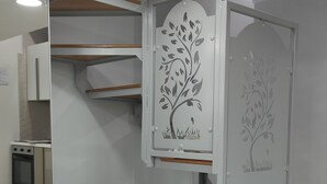 Ein modernes, kleines Zimmer mit integrierten Stauraumlösungen, einer kleinen Küchenzeile und einer dekorativen Baum-Applikation auf der Tür.