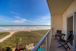 A balcony with a view of the beach, outdoor seating, and a pool area.