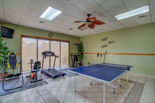 A fitness room with exercise equipment, a ping pong table, and motivational wall art.