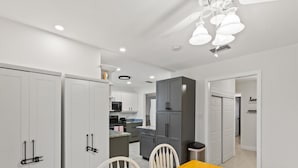 Cozinha moderna com armários brancos, uma mesa de jantar amarela e cadeiras brancas.