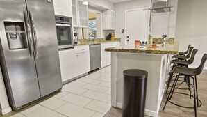 A modern kitchen with stainless steel appliances, a granite countertop, and a small bar area with stools.